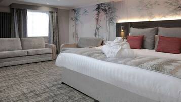 A hotel room with a bed, a sofa, a wall with a painting, and a window with curtains.