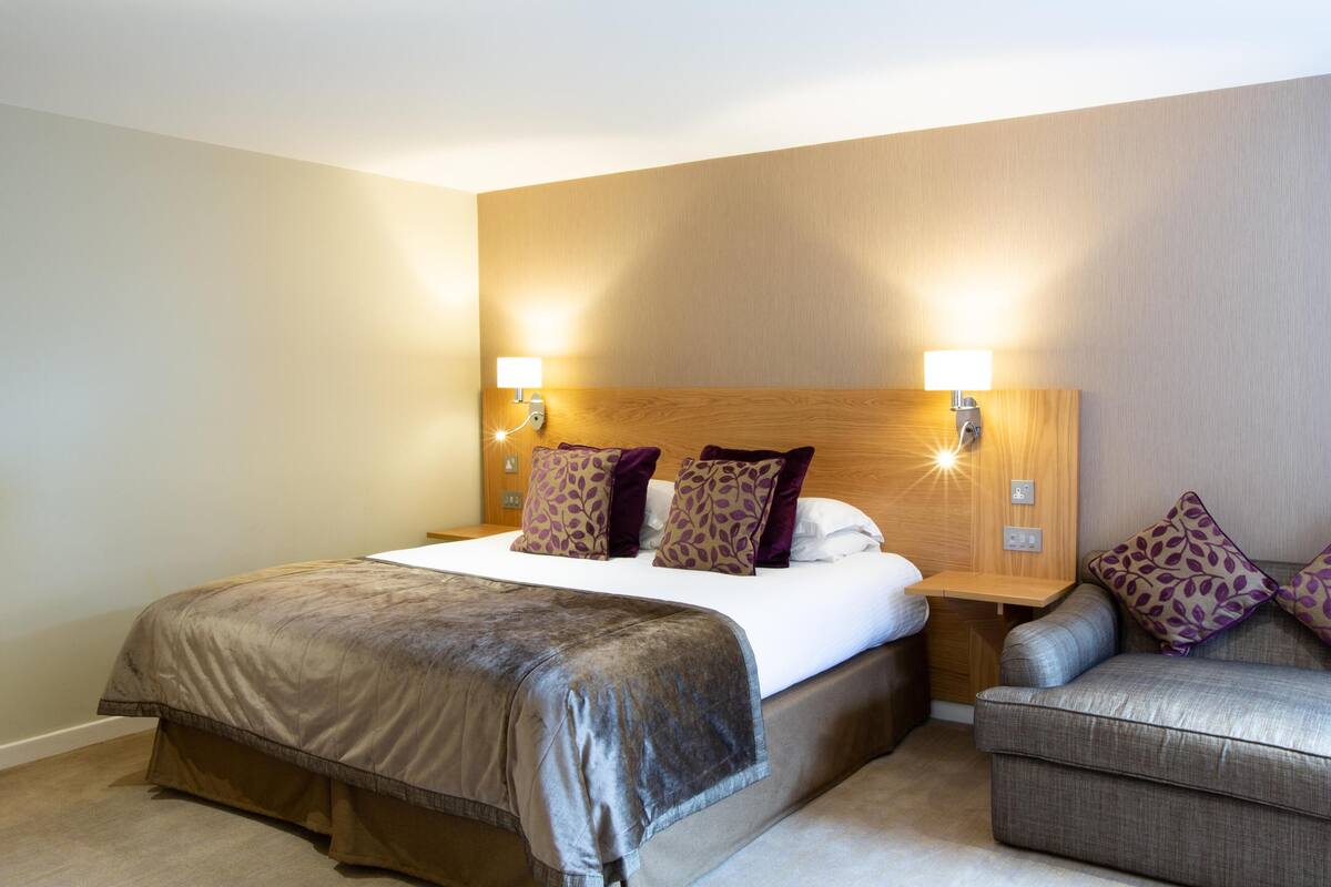A hotel room with a bed, two bedside lamps, a sofa, and a wooden headboard.