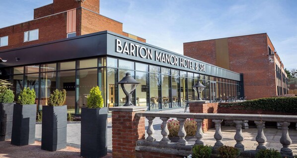The exterior of Barton Manor Hotel & Spa with a modern facade, large windows, and outdoor seating area.