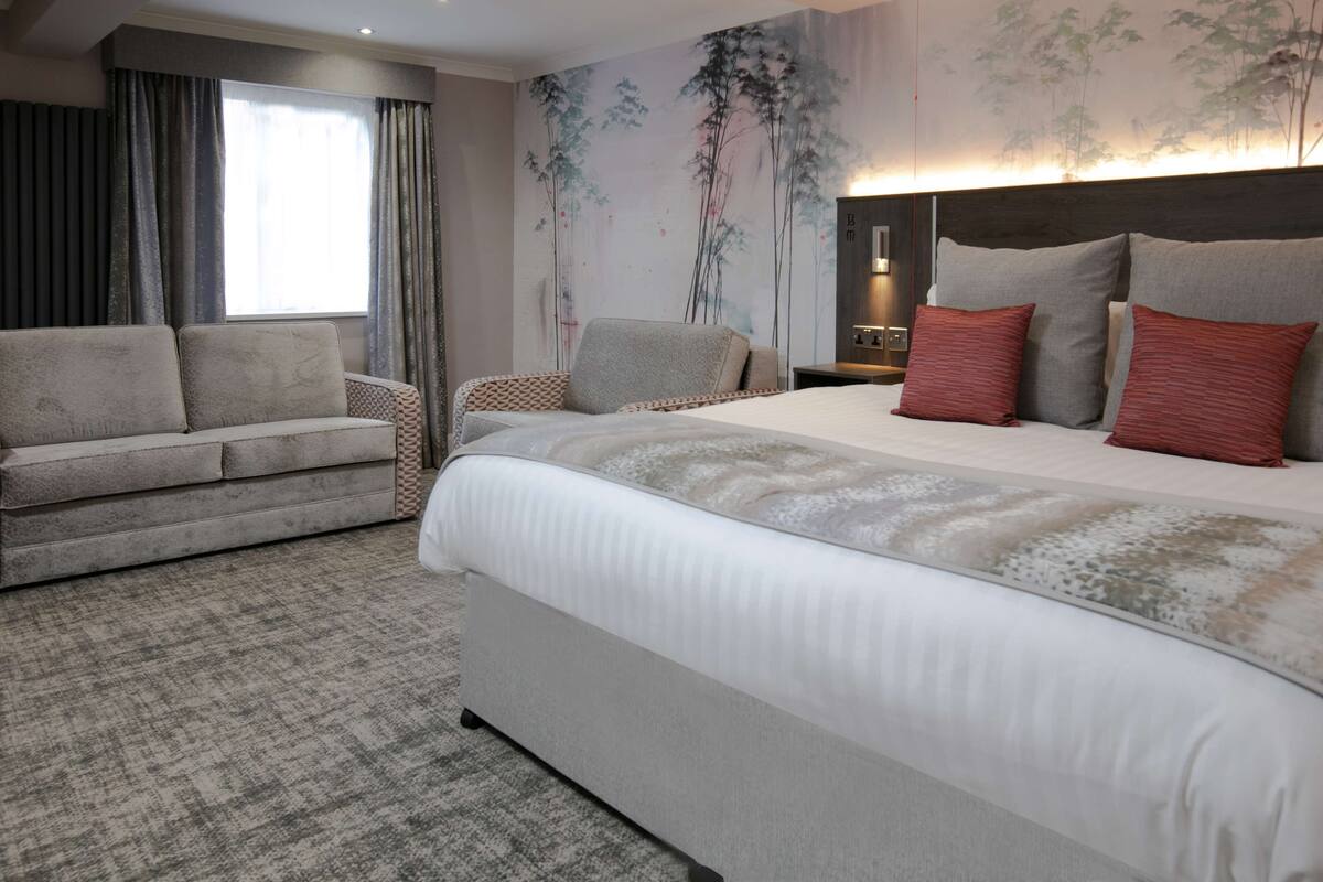 A hotel room with a large bed, a sofa, a nightstand, and a wall with a nature-themed mural.
