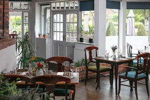 A restaurant with wooden tables and chairs, potted plants, and a view of the garden through large windows. - Barton Manor Hotel & Spa, BW Signature Collection (Preston)