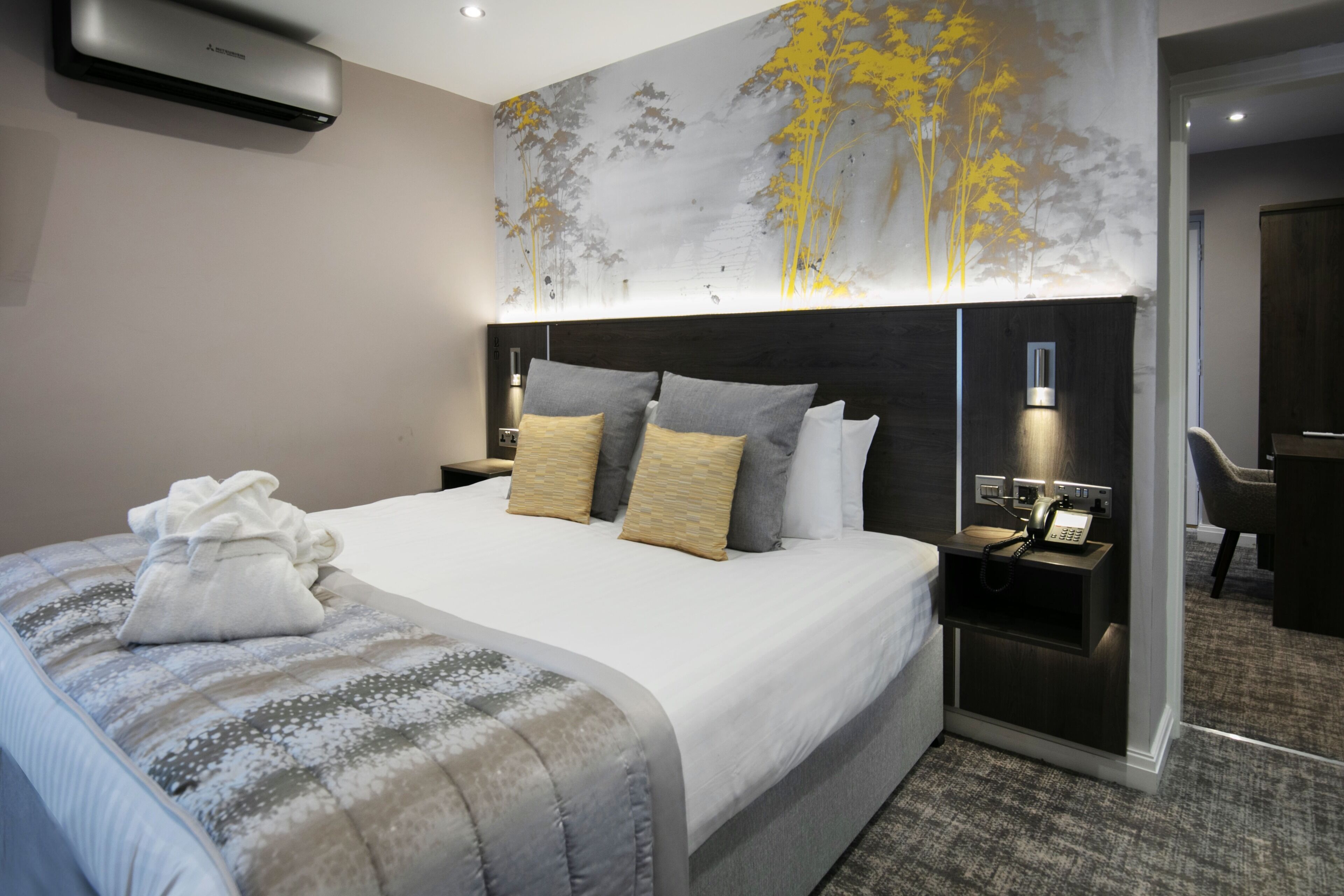 Una habitación de hotel moderna con una cama grande, una mesita de noche con teléfono y un aire acondicionado de pared.