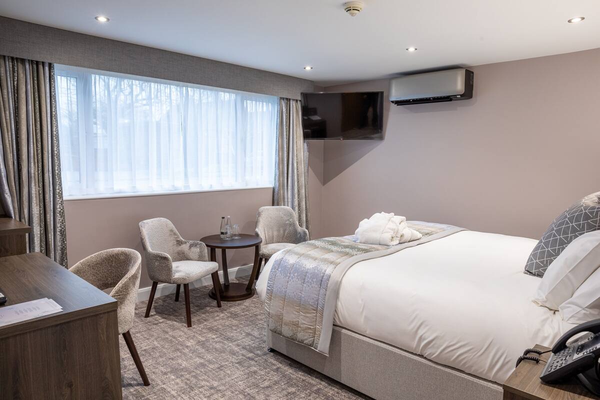 A hotel room with a large bed, a desk, a chair, a small table, and a TV mounted on the wall.