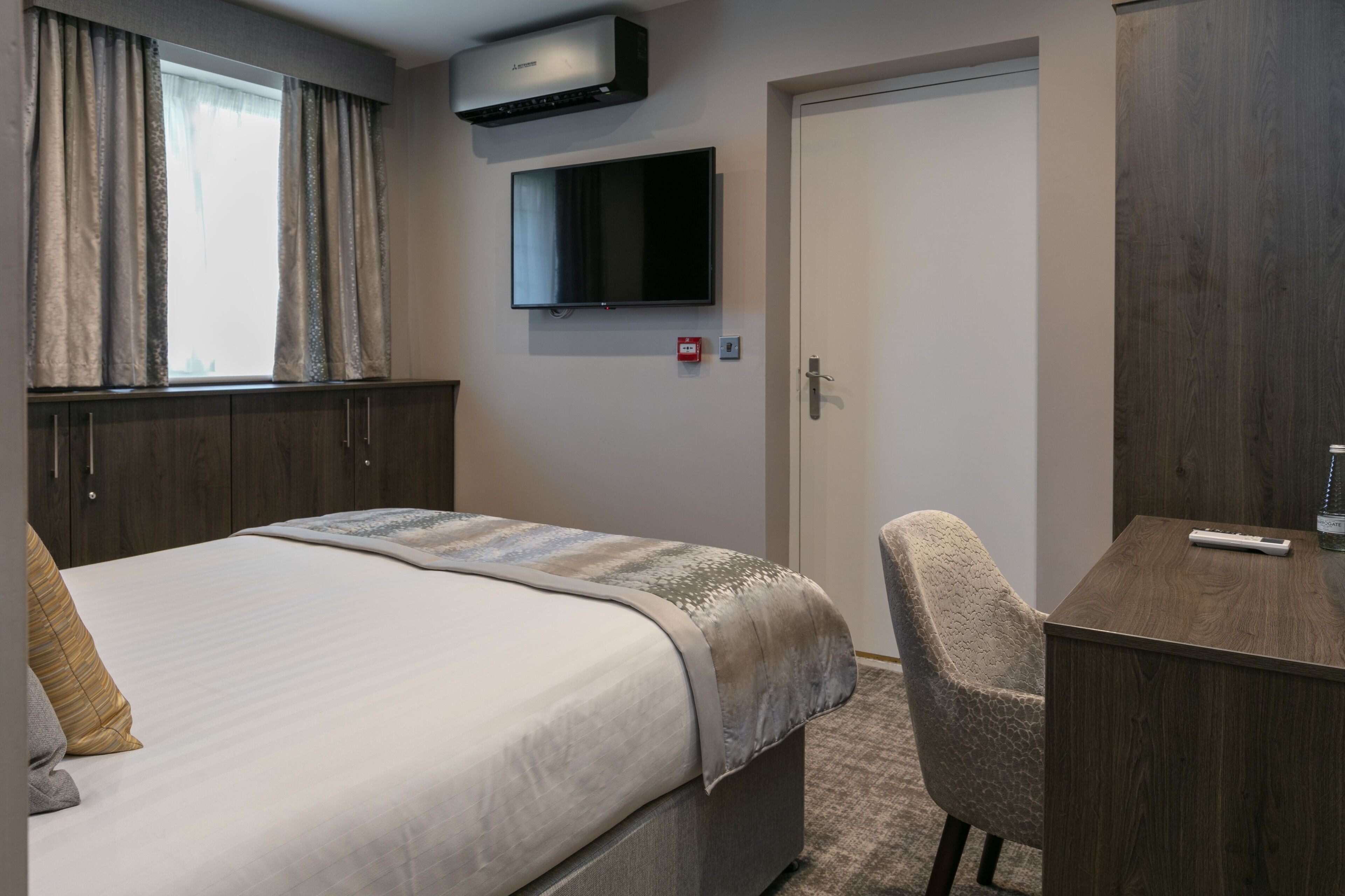 Una habitación de hotel con cama, escritorio, silla, televisión y armario.