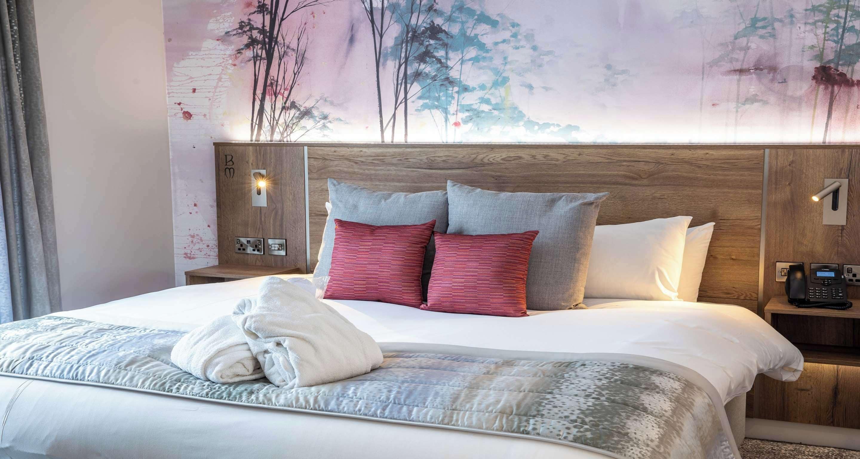 A hotel room with a neatly made bed, a wooden headboard, and a wall-mounted phone.