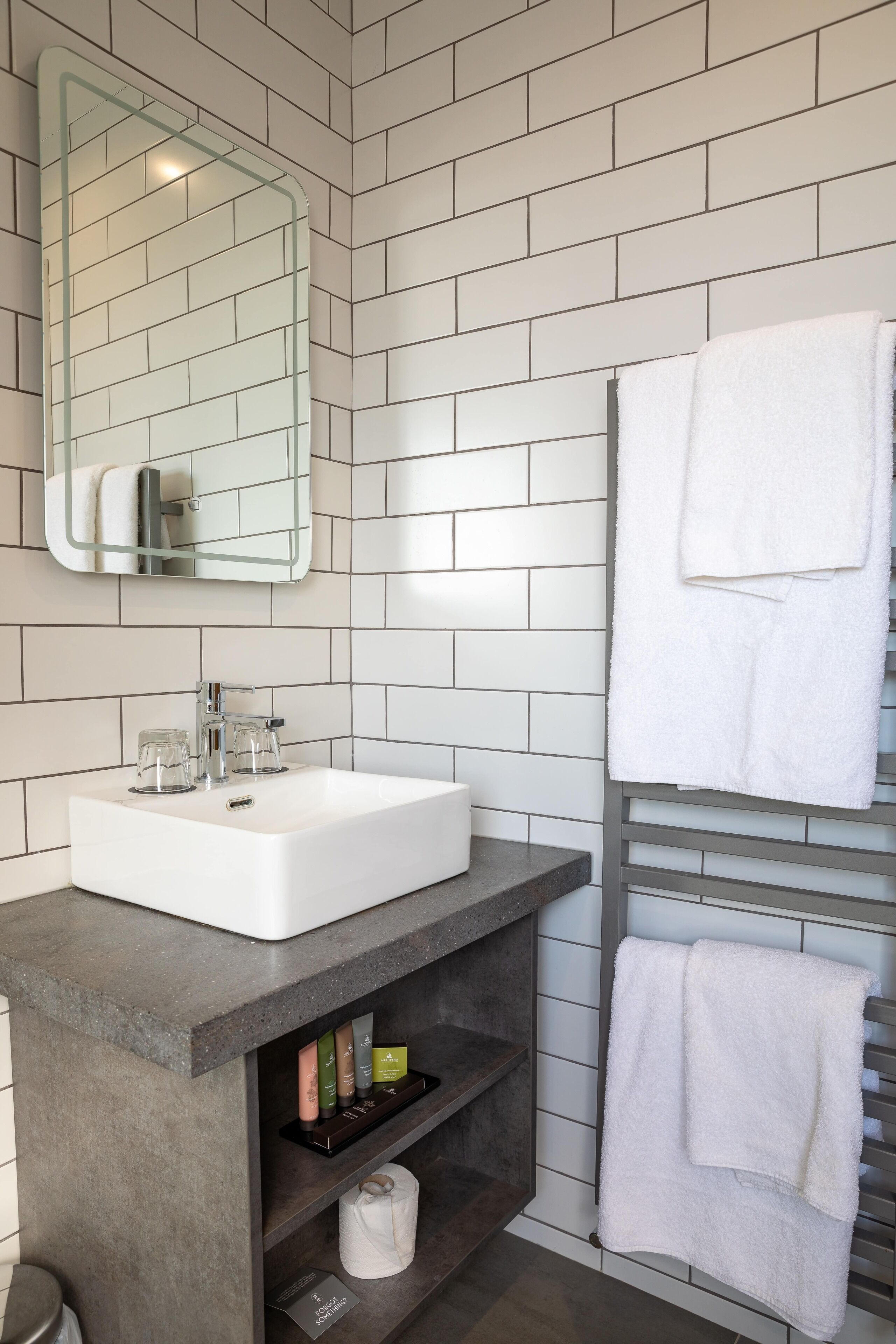 Un baño moderno con un lavamanos blanco, un espejo y un perchero para toallas.