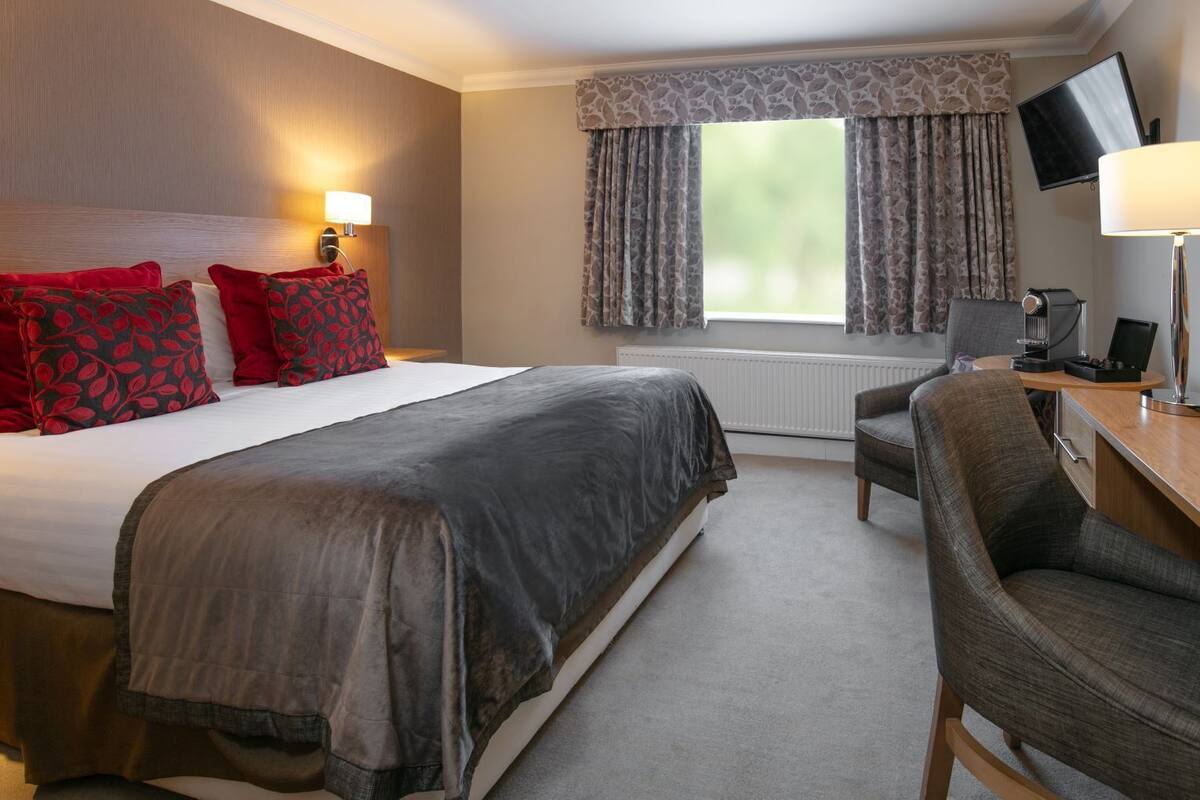 A hotel room with a large bed, a desk with a chair, a television, and a window with curtains.