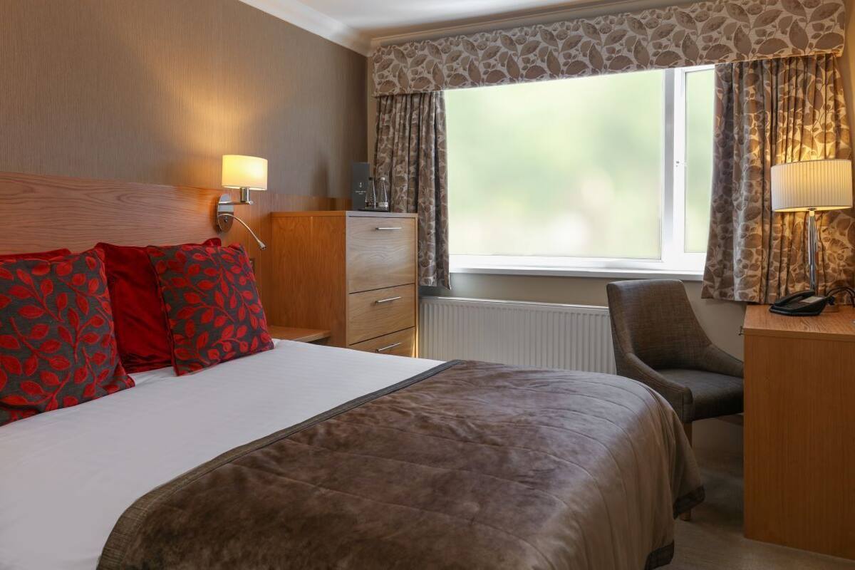 A hotel room with a bed, a desk, a chair, a lamp, and a window with curtains.