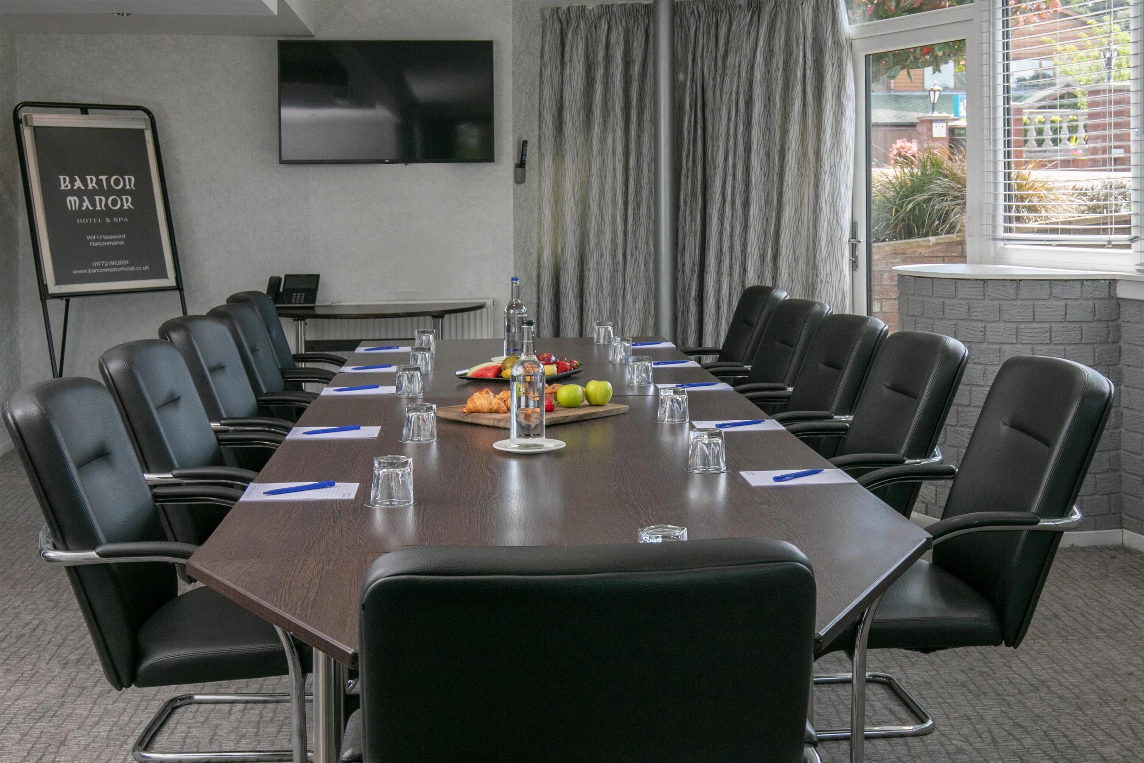 A conference room with a long table, chairs, a projector screen, and a banner.