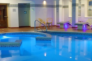 Una piscina con borde de mosaico azul, zona de ducha y asientos con luces de masaje.