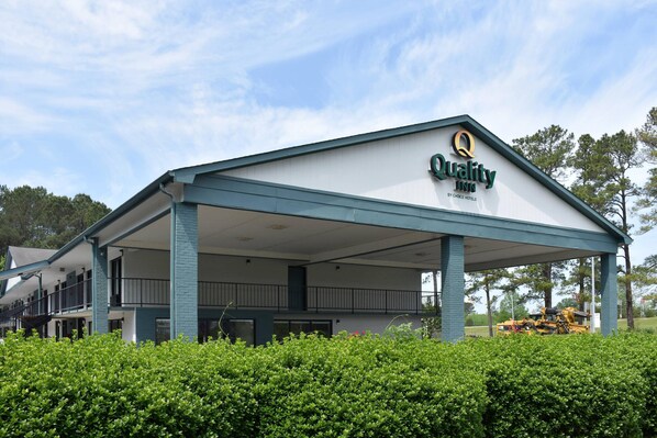 A hotel with a covered outdoor area, a sign indicating it is a Quality Inn by Choice Hotels, and a well-maintained lawn.
