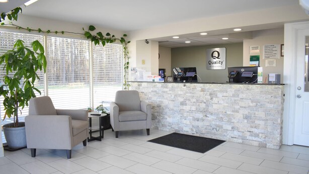 A reception area with a stone wall, two armchairs, a potted plant, and a reception desk with a computer and a sign that reads 'Quality.' - Quality Inn Manning I-95 (Manning)