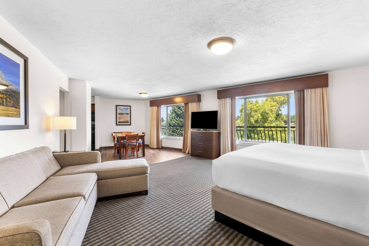 Une chambre d’hôtel comprenant un lit, un canapé, une télévision, un bureau et un balcon avec vue sur les arbres.