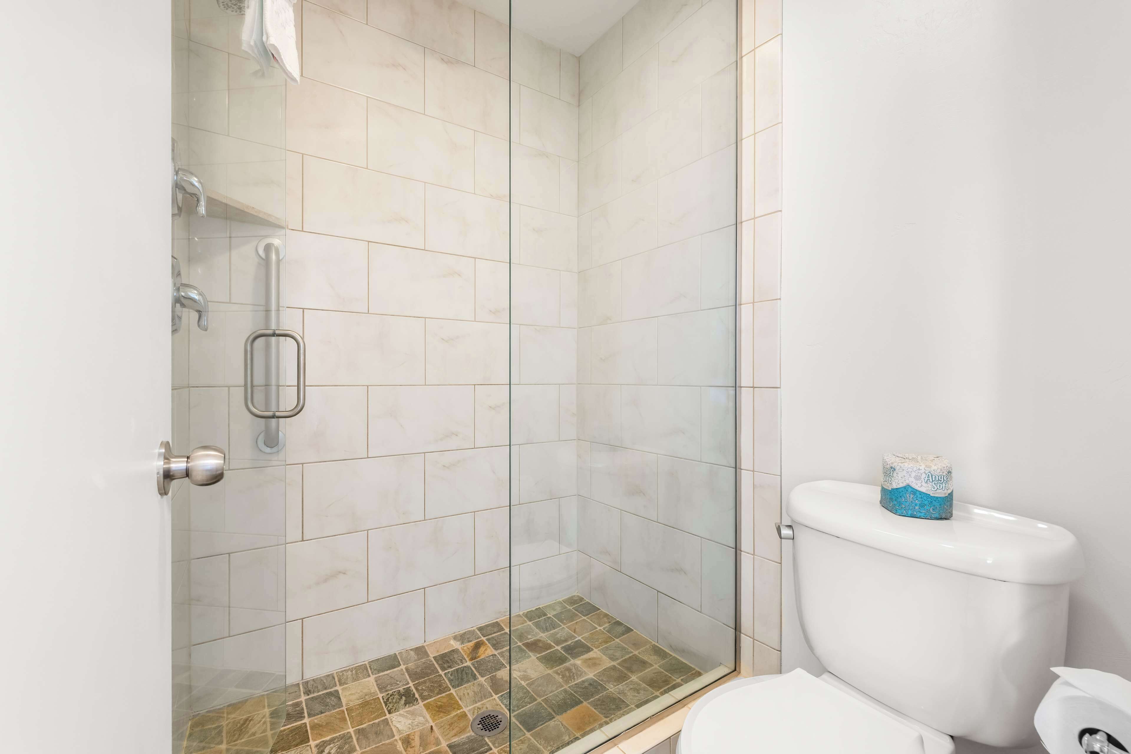 A bathroom with a glass-enclosed shower, a toilet, and a grab bar.