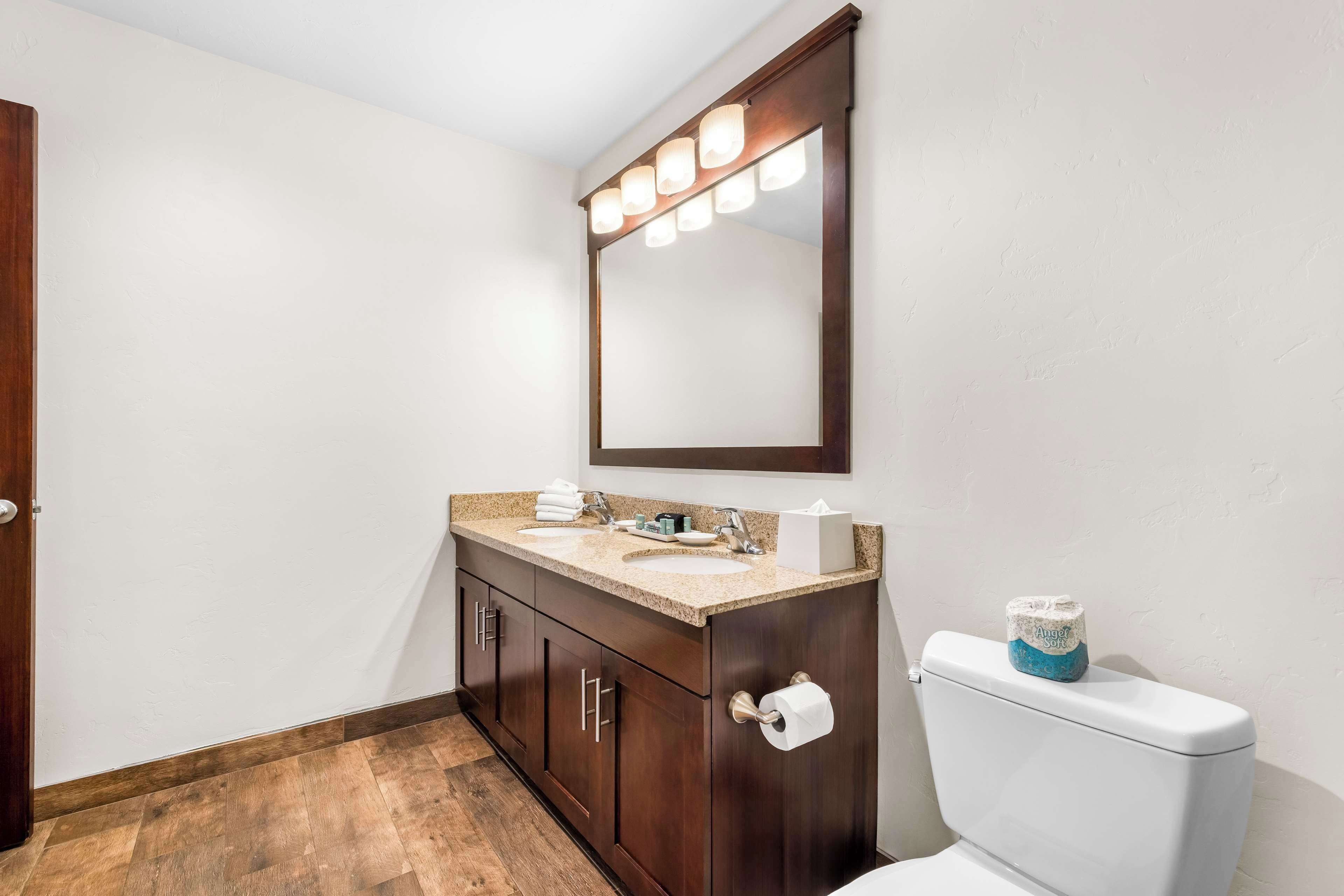 Un baño con tocador de madera, inodoro blanco y espejo con iluminación.