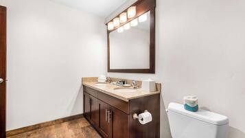 Un baño con tocador de madera, inodoro blanco y espejo con iluminación.