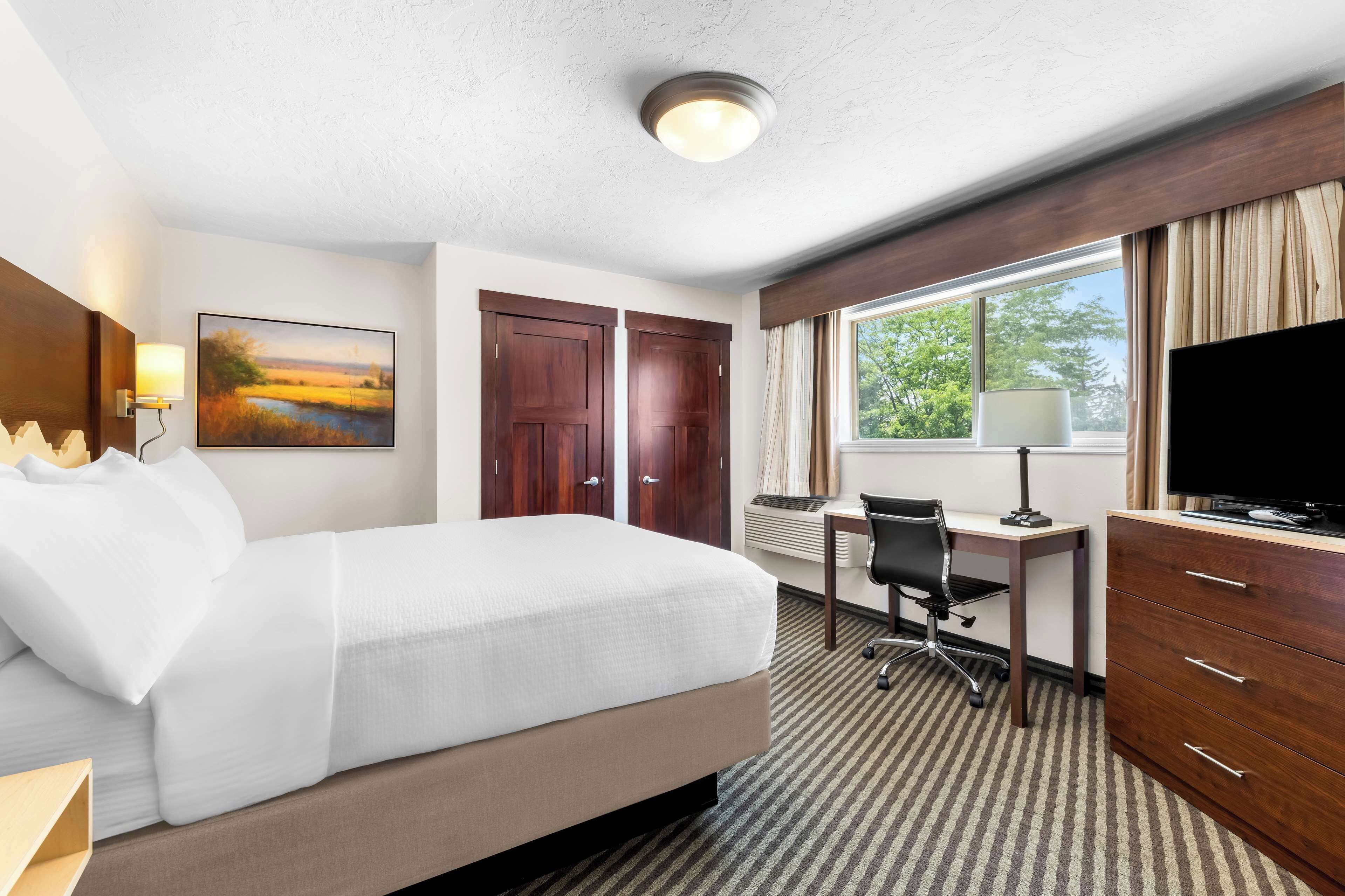 Una habitación de hotel con cama, escritorio, televisión y ventana con cortinas.
