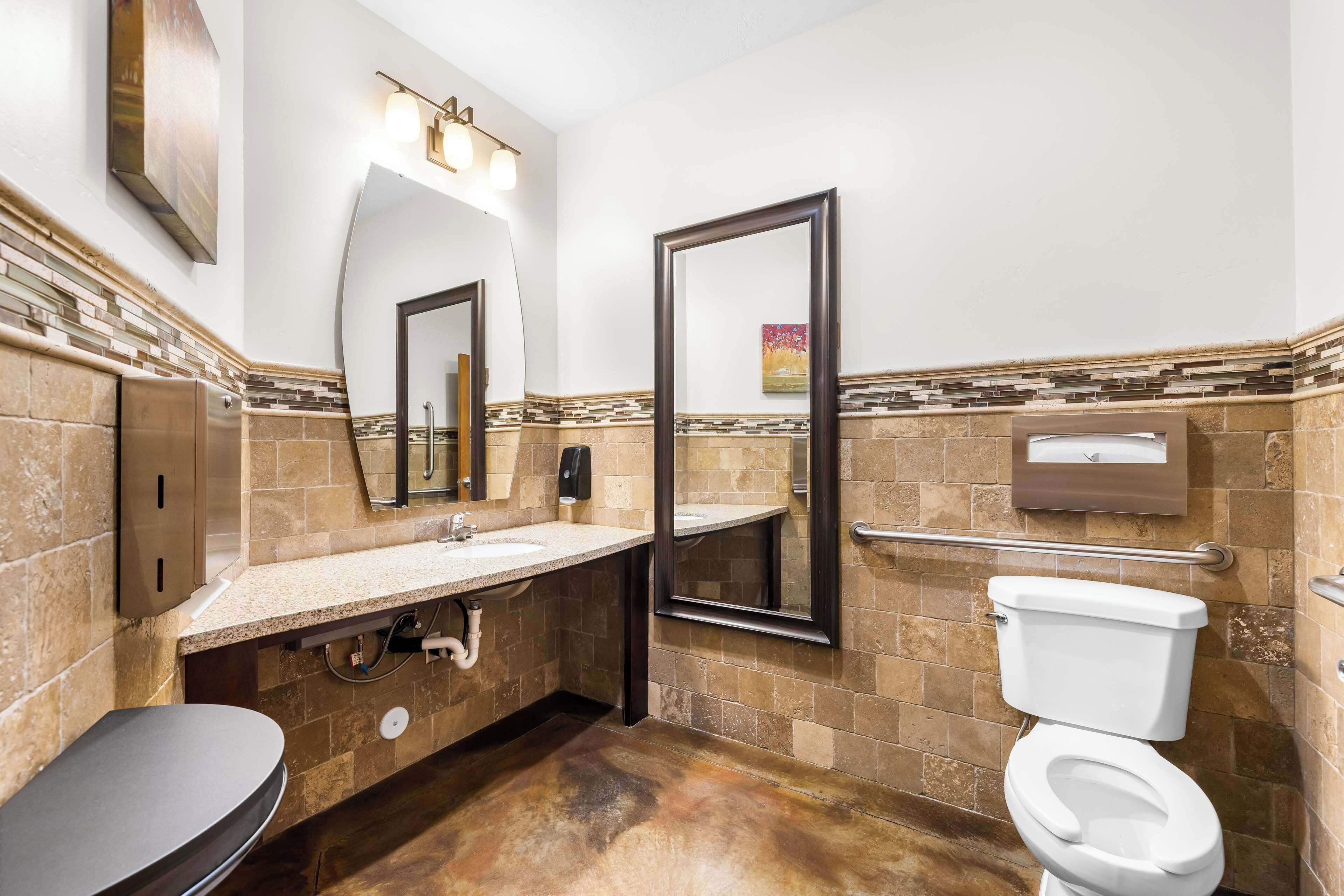 A bathroom with a sink, mirror, toilet, and towel dispenser.