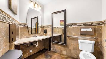 A bathroom with a sink, mirror, toilet, and towel dispenser.