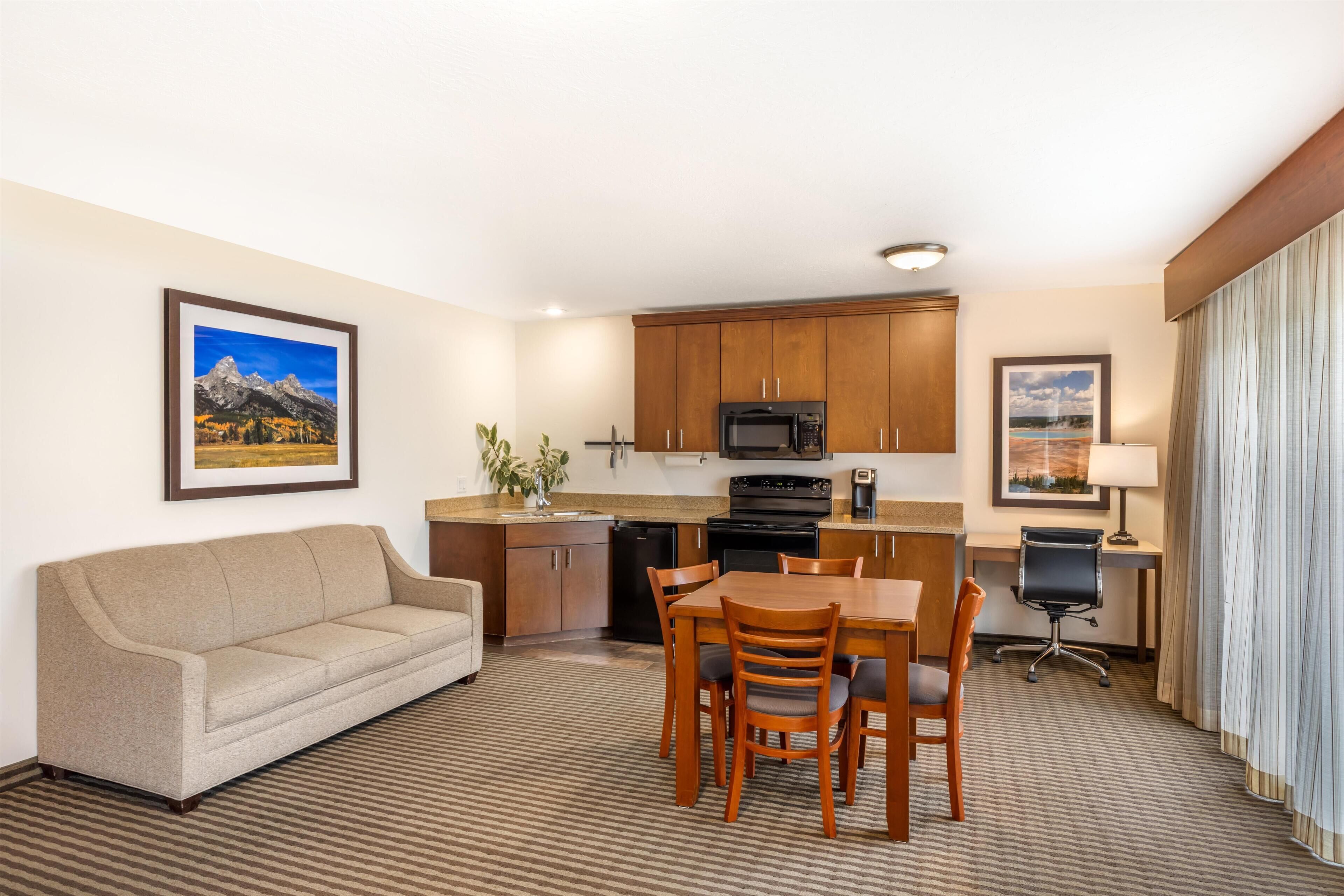 Habitación de hotel con sof á, mesa de comedor, sillas, zona de cocina con microondas y un pequeño espacio de trabajo.