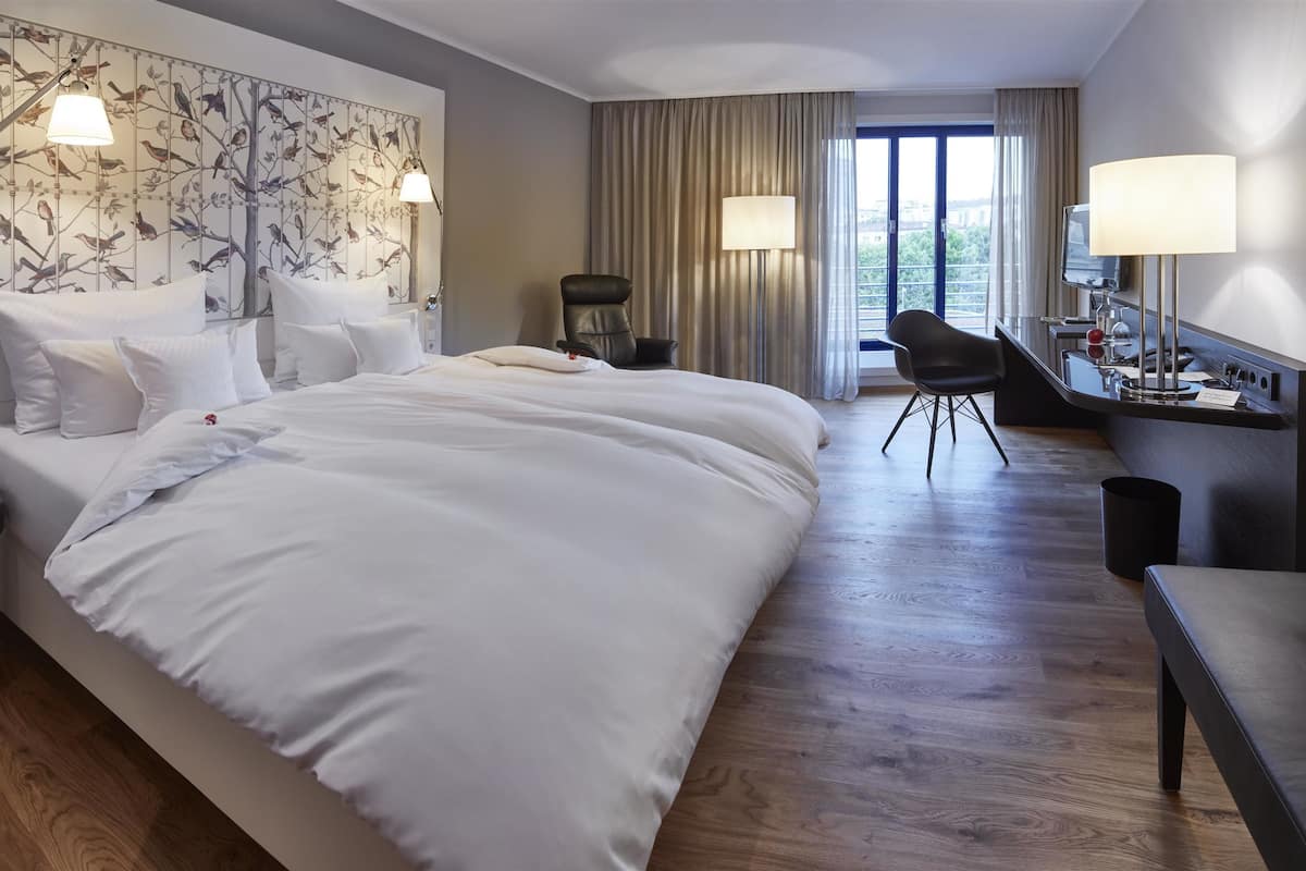 Une chambre d’hôtel avec un grand lit, un bureau, une chaise et une vue sur l’extérieur.