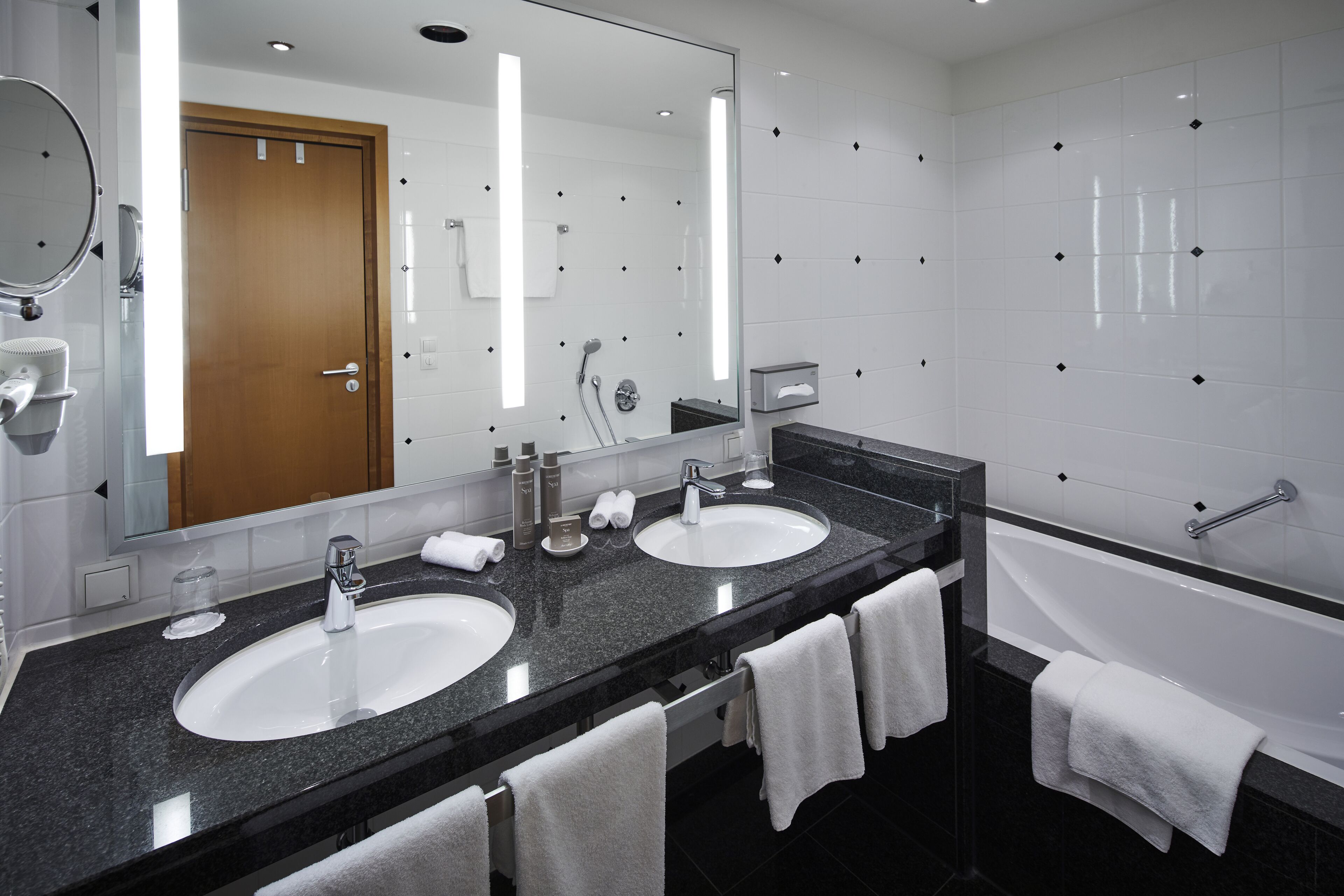 Un baño moderno con dos lavamanos, un espejo grande y una bañera.