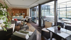 A modern hotel lobby with wicker furniture, a reception desk, and large windows offering views of the city. - Parkhotel Pforzheim (Pforzheim)