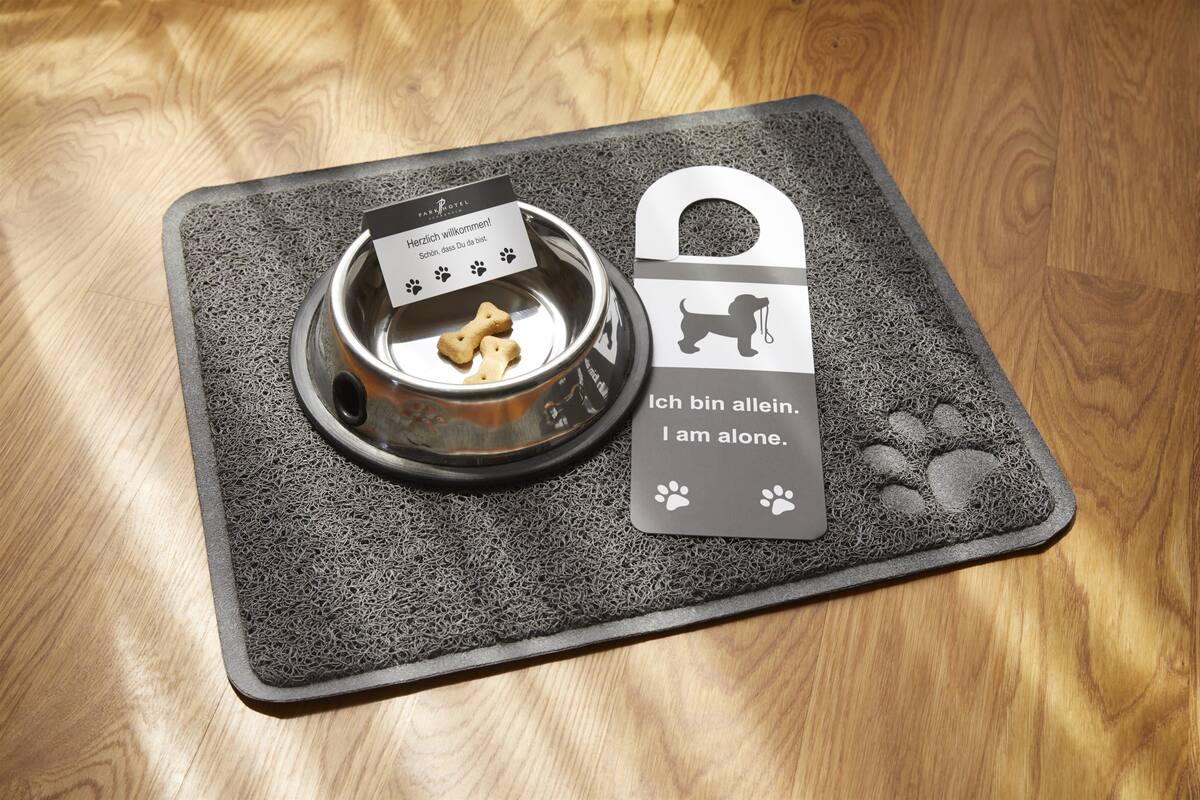 Una cama para mascotas con un tazón metálico y una etiqueta que dice "Ich bin allein. I am alone."