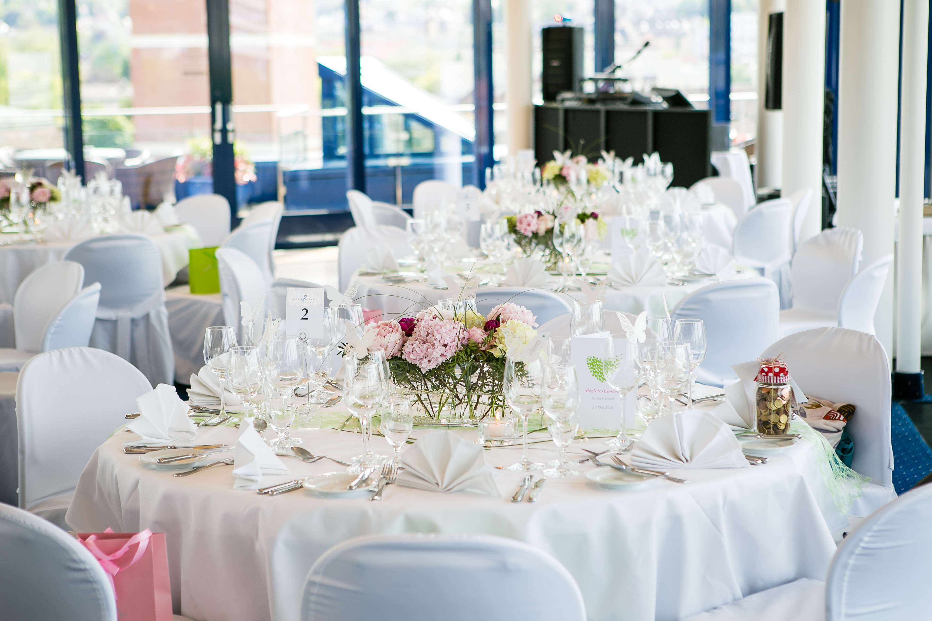 A banquet hall with round tables set for a formal event, featuring white tablecloths, floral centerpieces, and neatly arranged tableware.