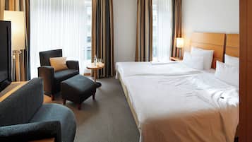 A hotel room with a large bed, a sofa, a chair, a small table, and a television.