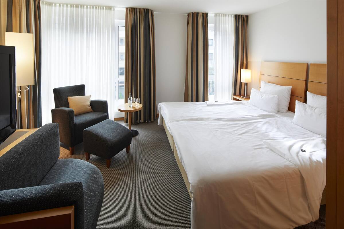 Une chambre d’hôtel avec un grand lit, un canapé, une petite table avec une lampe et des rideaux.