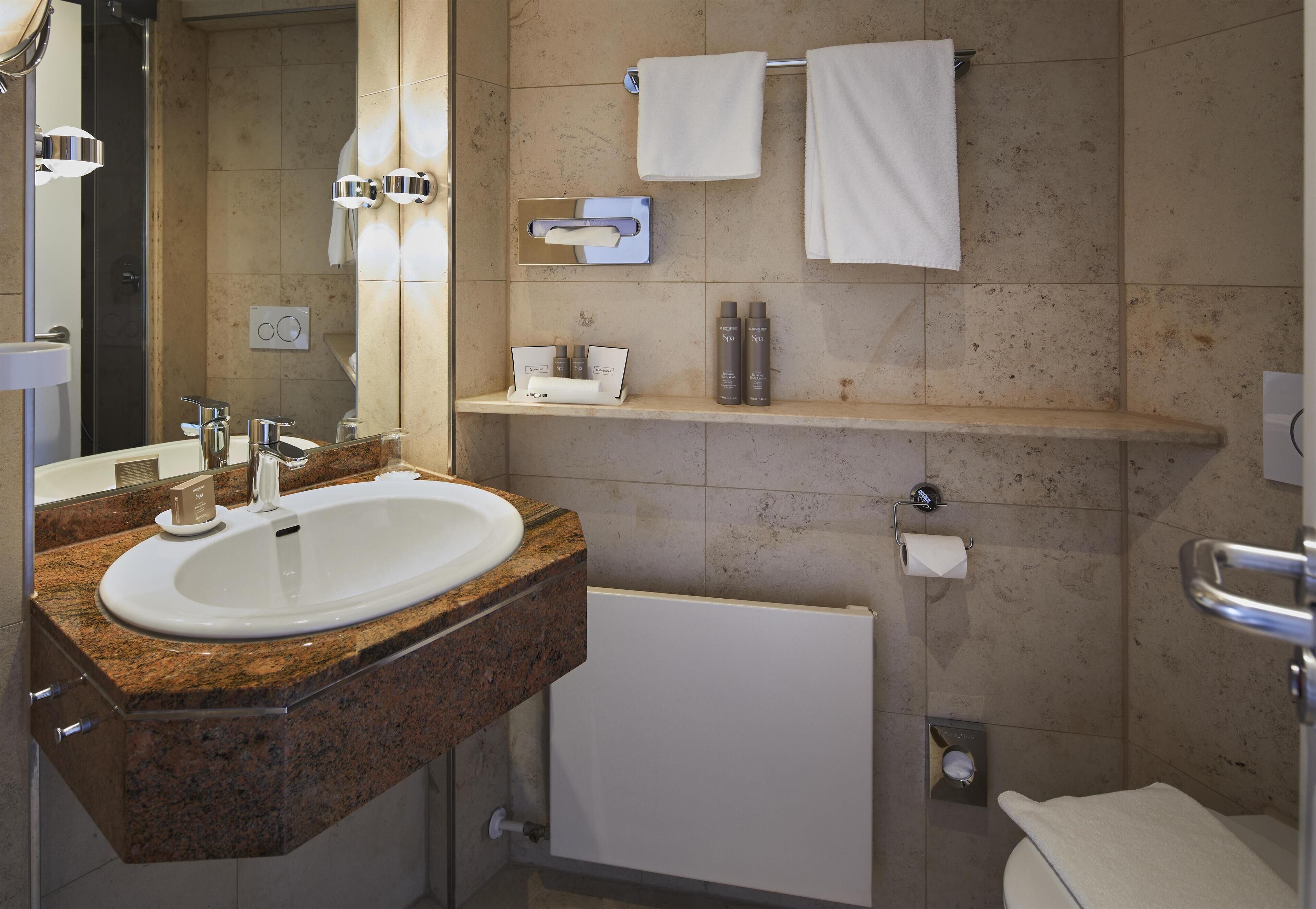 Un baño moderno con lavamanos de granito, un espejo, un perchero y una estantería con artículos de aseo.