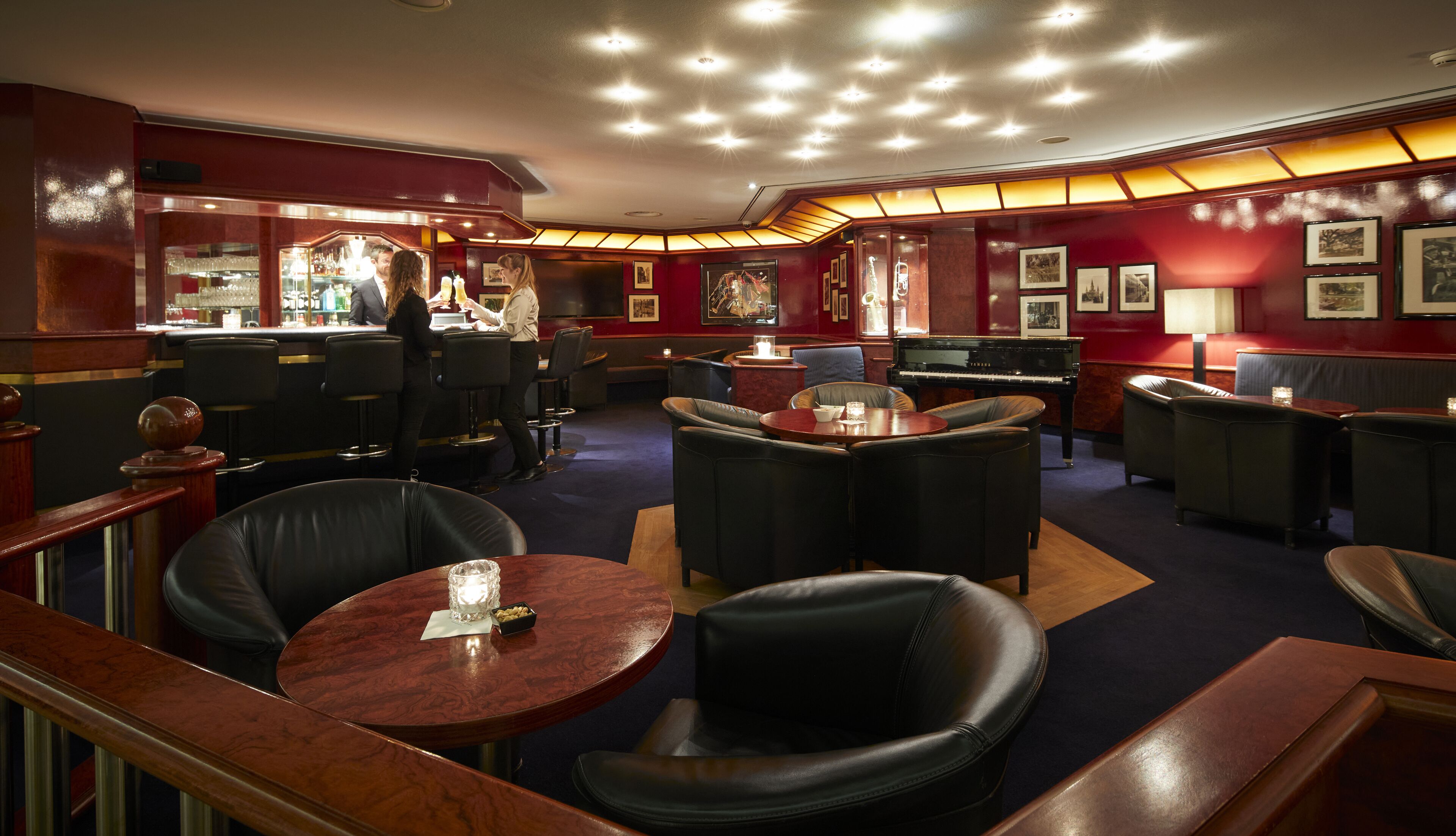 A bar area with leather seating, a piano, and framed pictures on the walls.