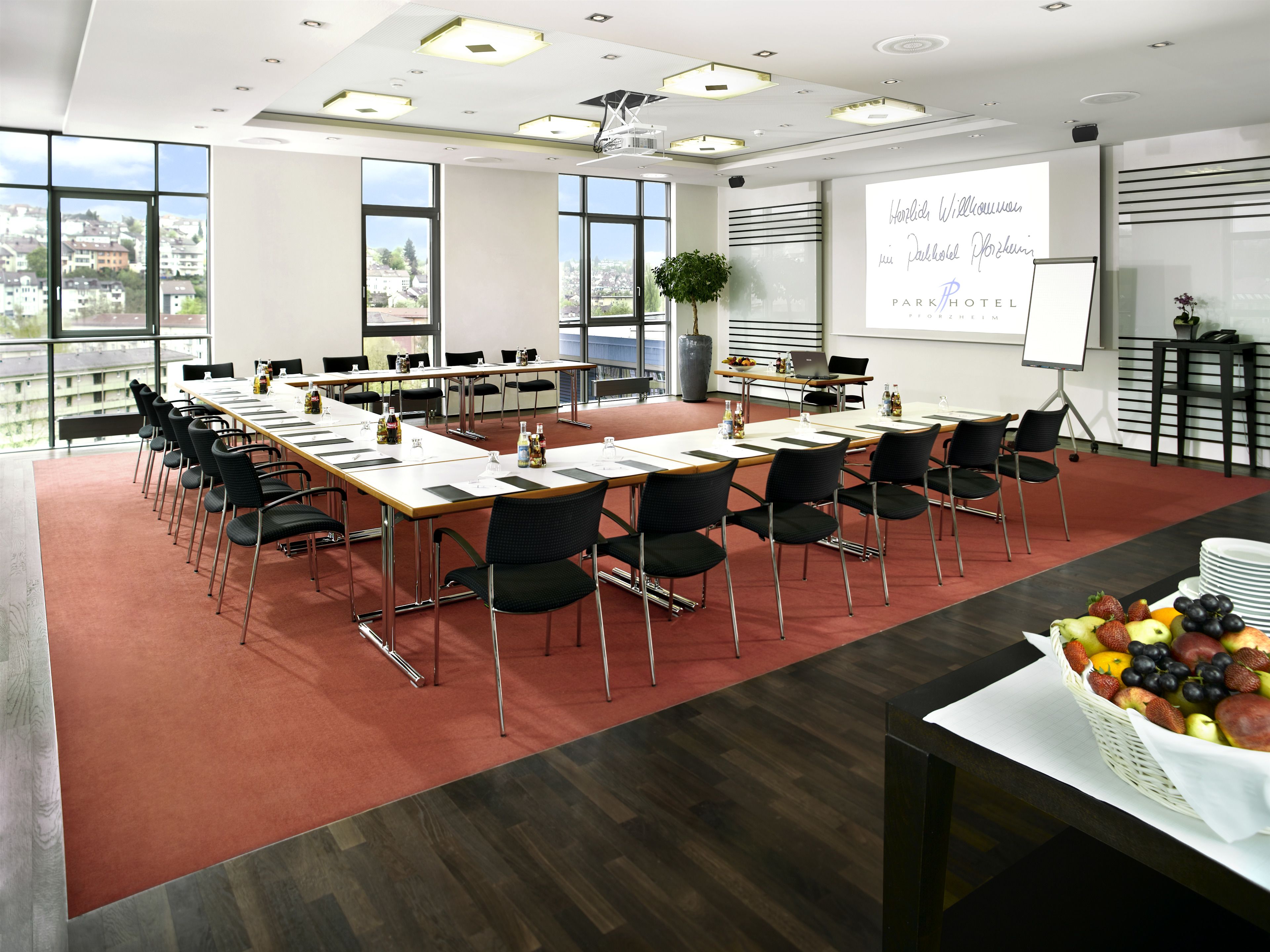 A conference room with a long table, chairs, a projector screen, and a fruit basket.