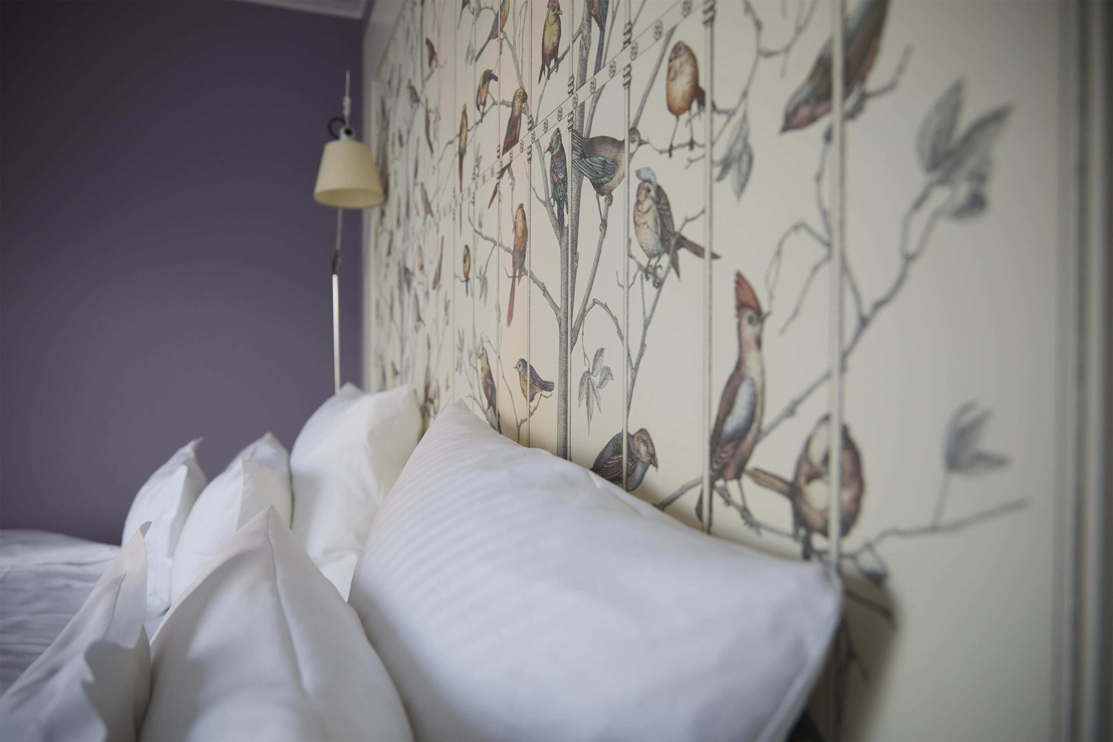 Een bed met witte beddengoed en een muur met behang met een vogelmotief.