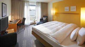 A hotel room with a large bed, a desk with a chair, a television, and a window with curtains.