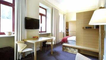 Een hotelkamer met een bed, een bureau met stoel, een televisietoestel en een lamp.