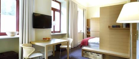 Habitación de hotel con cama, escritorio, silla, televisor y lámpara.