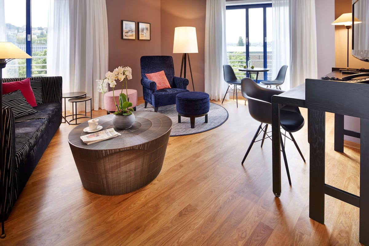 Une chambre d’hôtel moderne équipée d’un canapé, d’un fauteuil, d’une table basse ronde, d’une table à manger et de chaises.