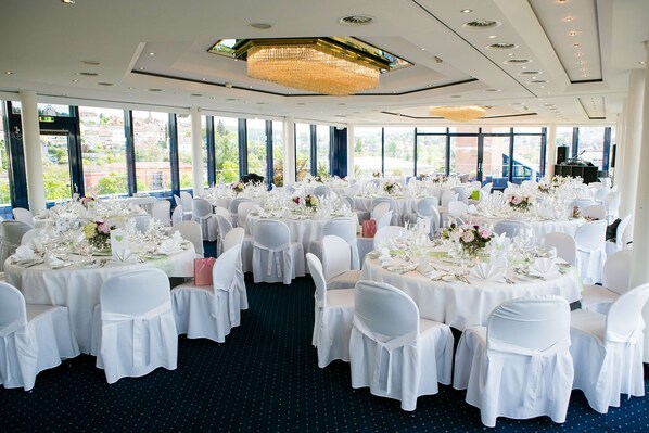 Un salón de banquetes con mesas redondas, sillas blancas y una araña.