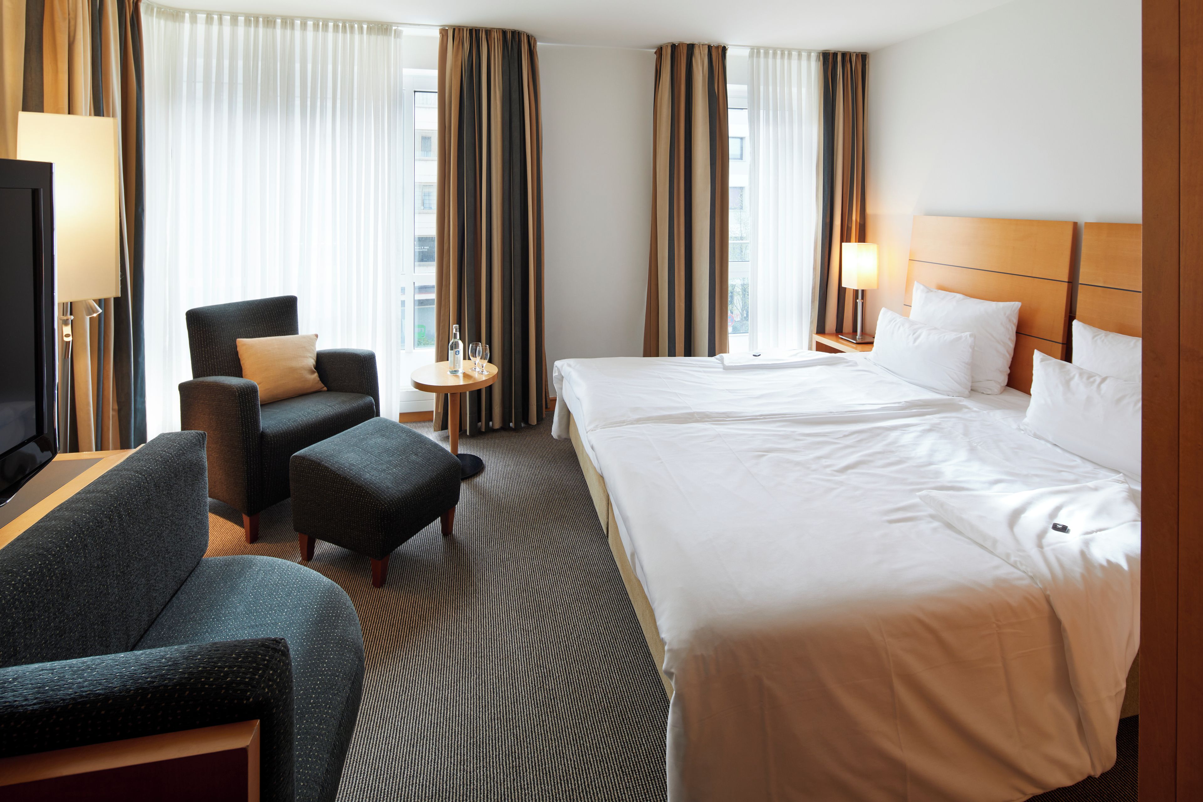 Ein Hotelzimmer mit einem großen Bett, einer Couch, einem Sessel, einem kleinen Tisch und einem Fernseher.