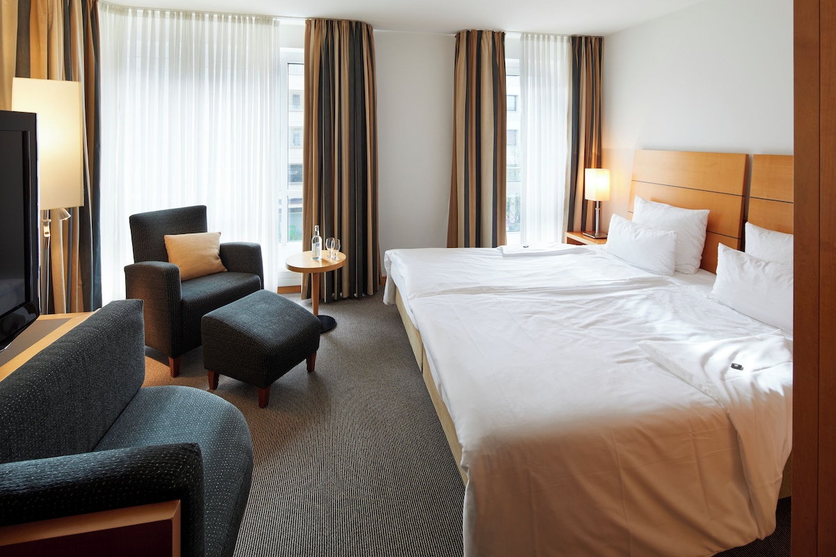 Habitación de hotel con una cama grande, un sofá, una silla, una mesita y un televisor.