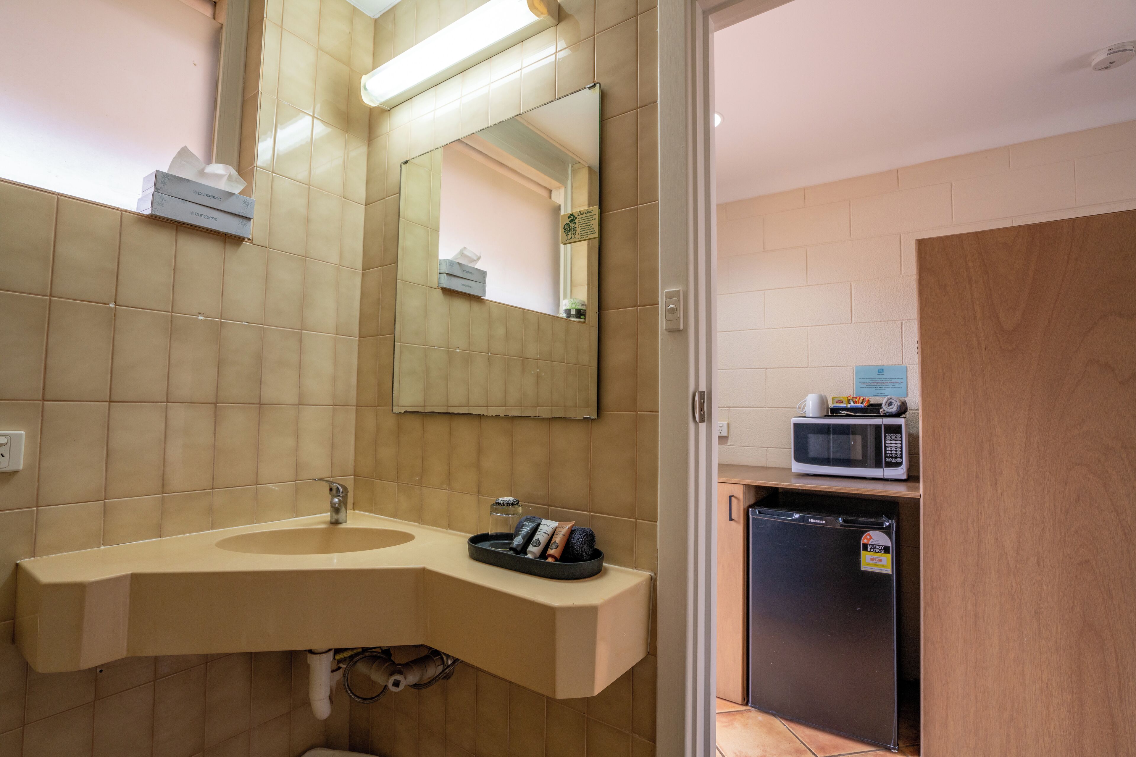 A modern bathroom with a sink, mirror, and a microwave on a shelf.