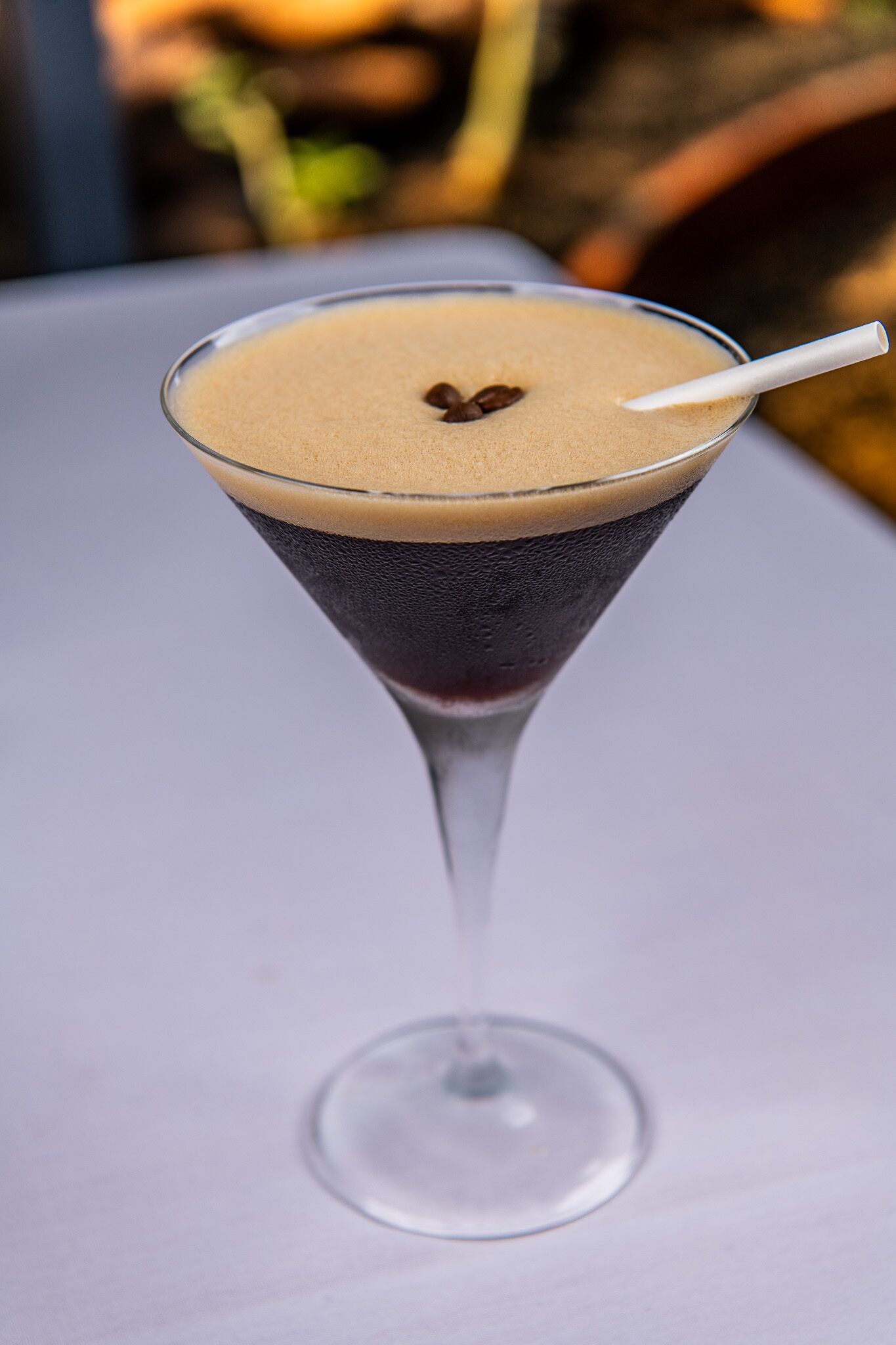 Una copa de martini con una bebida en capas sobre una mesa blanca.
