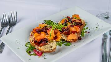 A rectangular white plate with a food item topped with orange segments, dried cranberries, and greens, accompanied by cutlery on a white tablecloth.