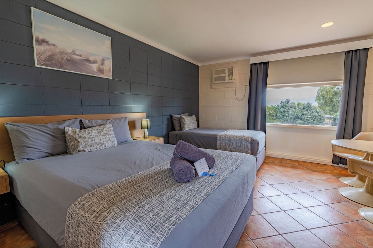 A hotel room with a large bed, a smaller bed, a desk, and a window with curtains.
