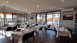 A restaurant with multiple tables set for dining, large windows offering a view of the outside, and a modern interior design. - Hospitality Port Hedland (Port Hedland)