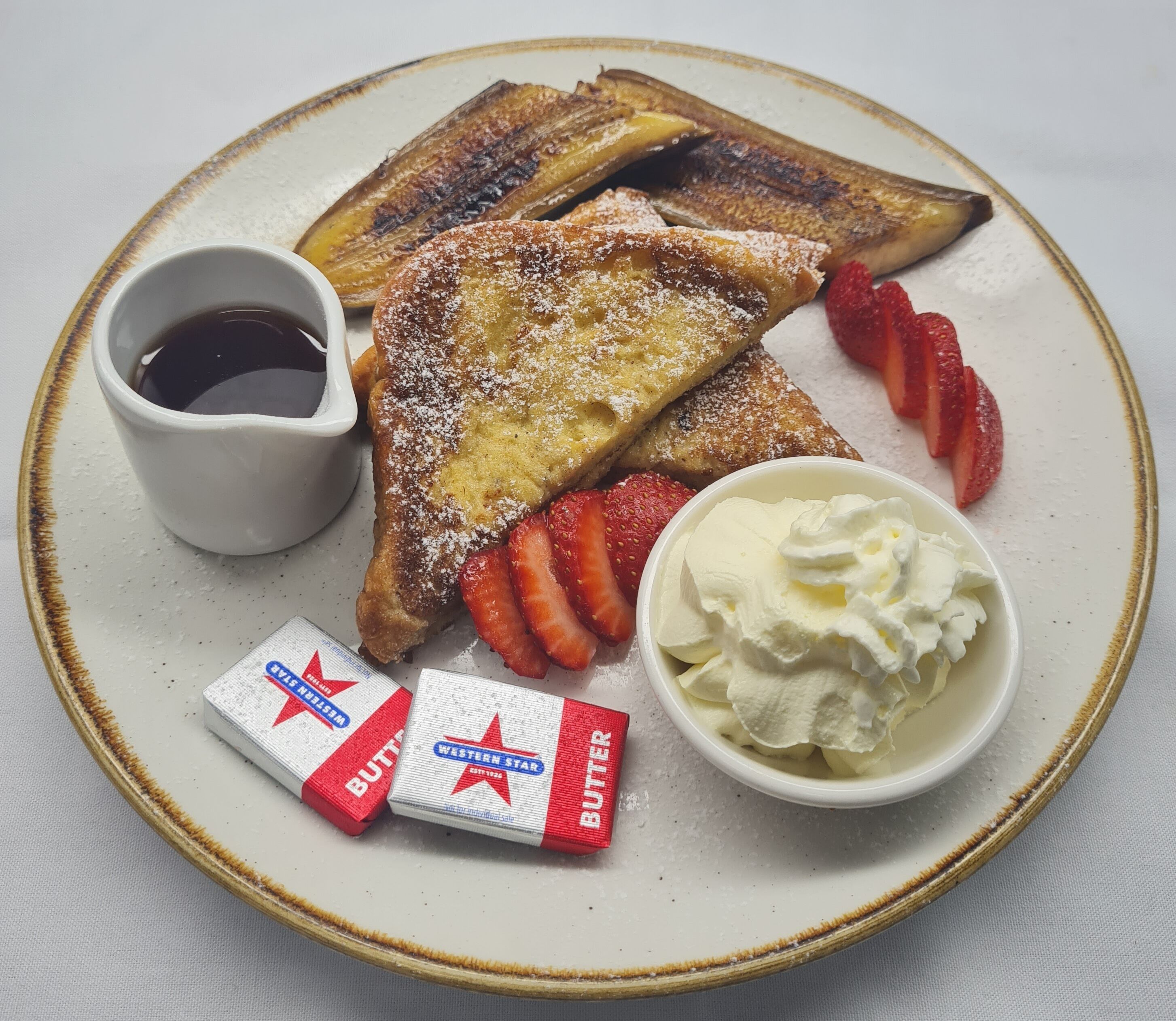 Une assiette de pain perdu, de fraises, de crème fouettée et de petits paquets de beurre.