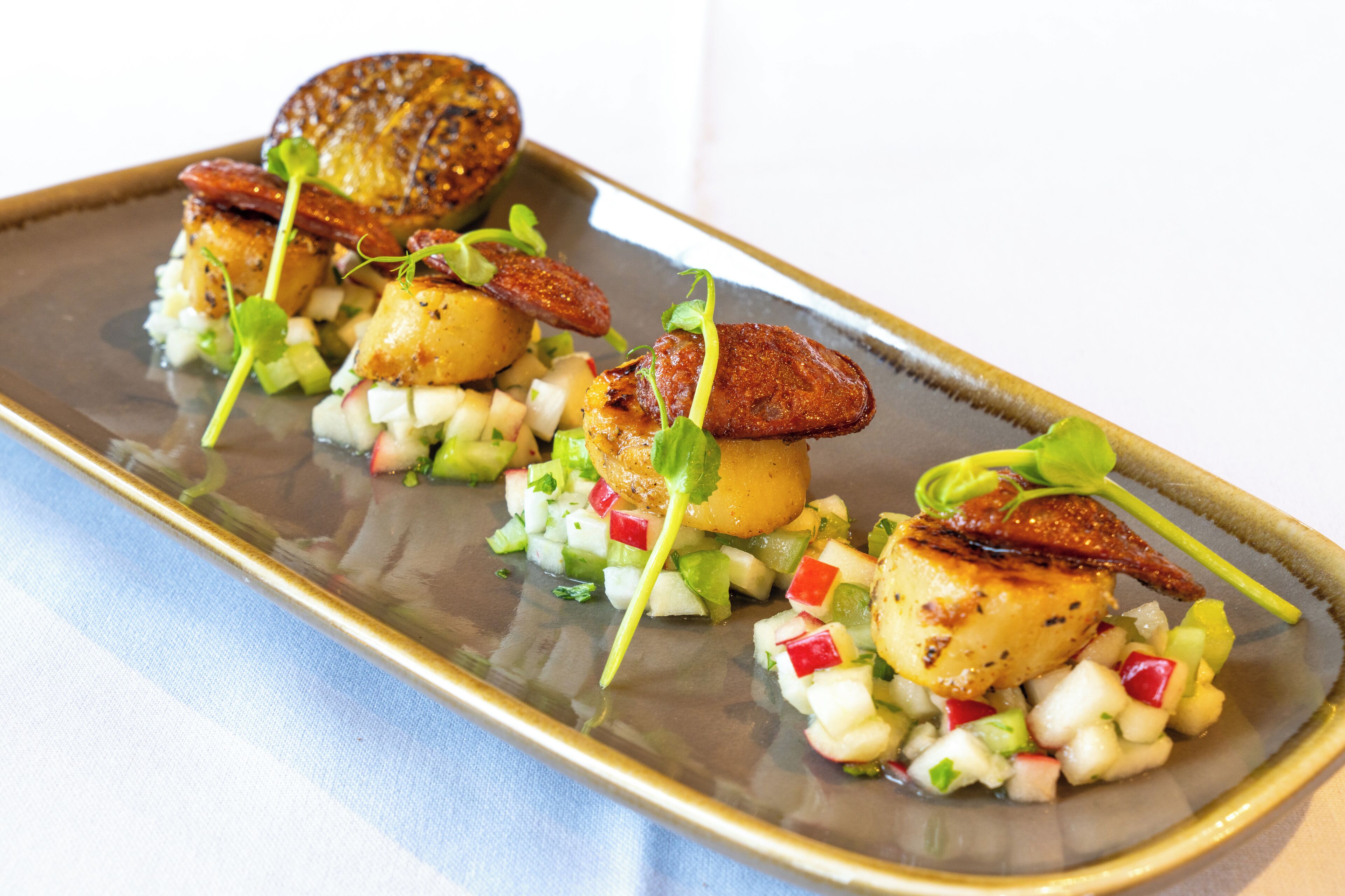 A plated dish with seared scallops, potatoes, and a diced vegetable medley.