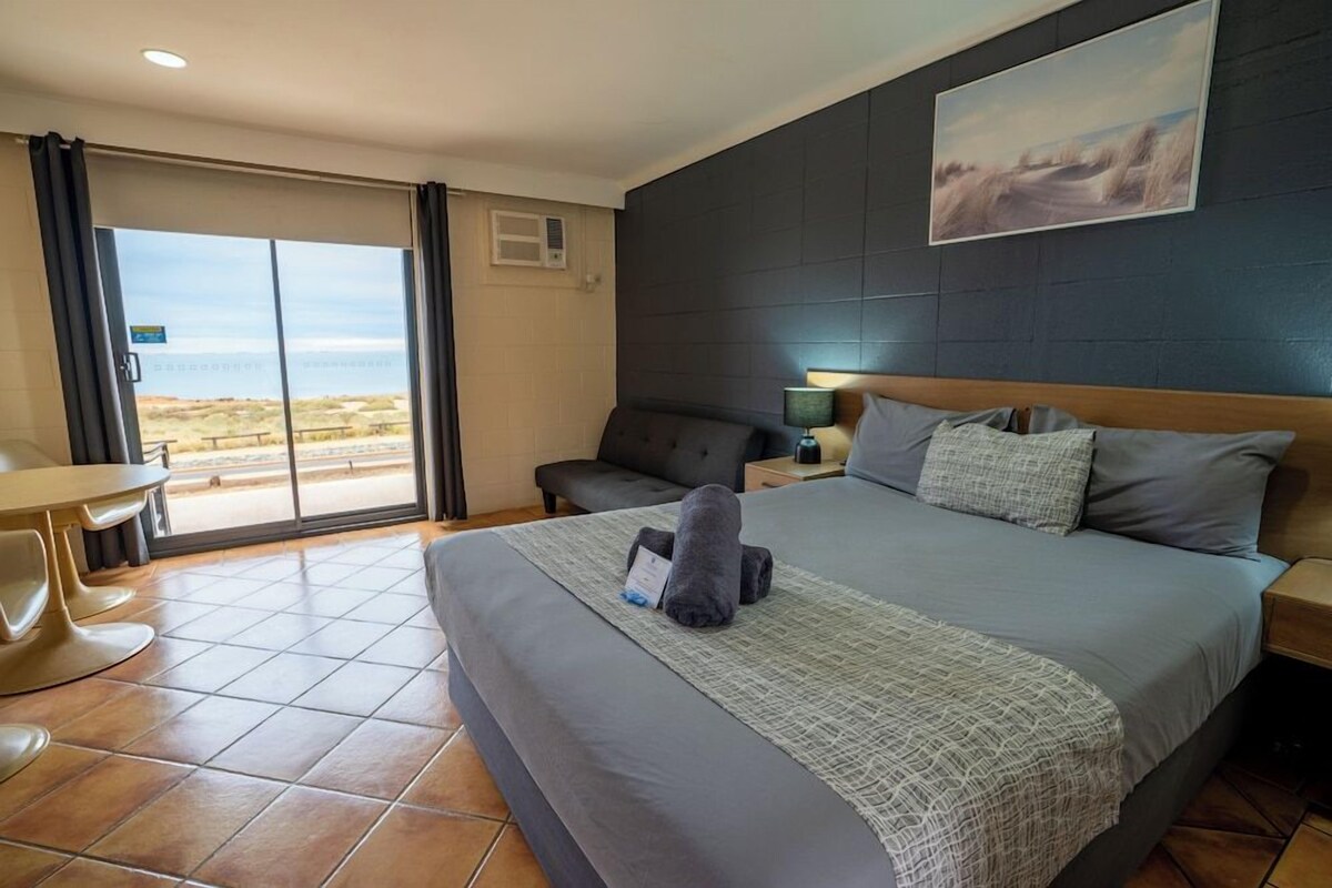 A hotel room with a large bed, a desk, a chair, and a view of the outdoors.